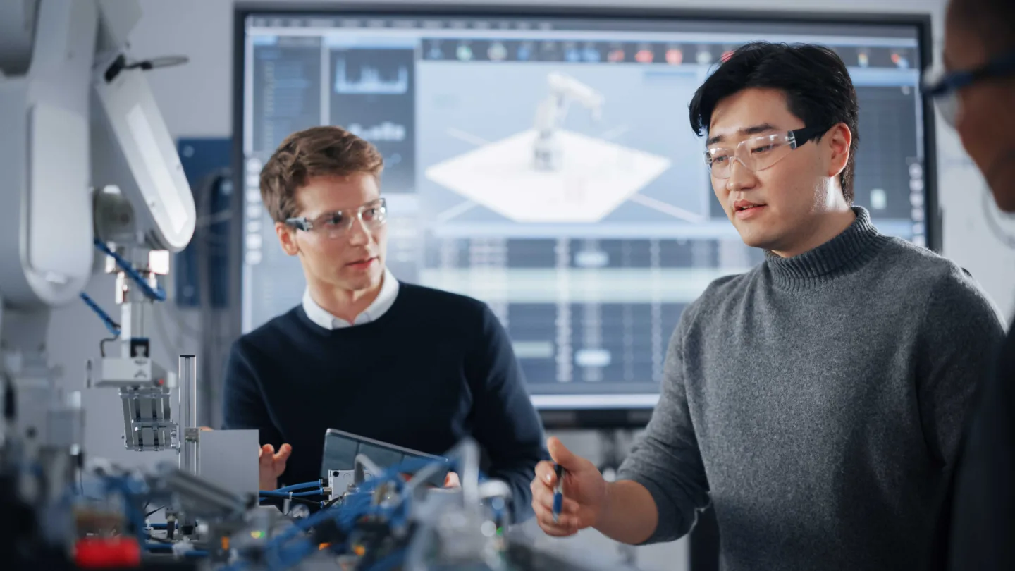 Personer som studerar till Technical Sales Manager står vid en industrirobot.